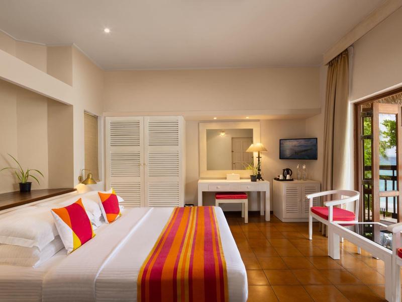 Helles Schlafzimmer mit großem Bett, weißen Möbeln, bunten Kissen und Zugang zu einem Balkon.