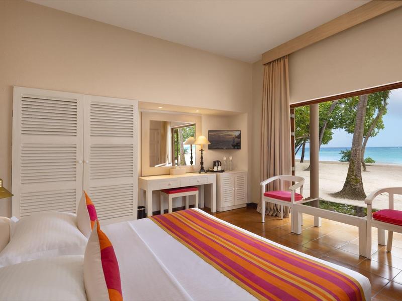 Helles Schlafzimmer mit großem Bett, Fensterfront zum Strand und Meer, weißer und rot-orangefarbener Dekor.