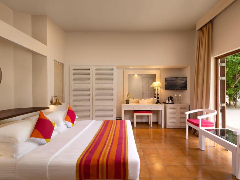 Helles Schlafzimmer mit großem Bett, bunten Kissen, Schreibtisch, Stuhl und Zugang zum Garten.