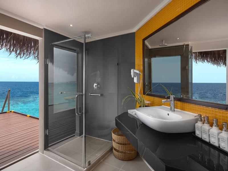 Moderner Badezimmerecke mit Glasdusche, schwarzer Theke, Waschbecken und Meerblick durch offene Tür.