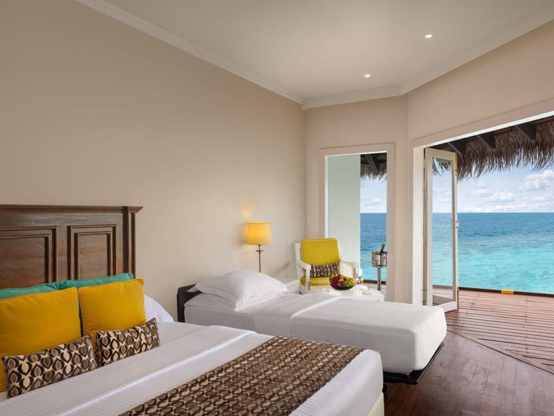 Modernes Hotelzimmer mit zwei Betten, gelben Akzenten und Meerblick durch große Fenster.