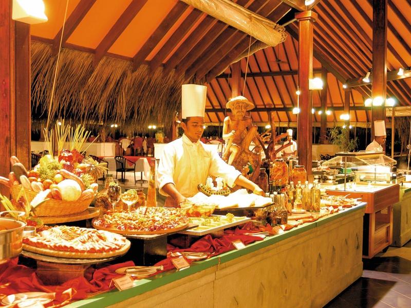 Buffet mit vielfältigen Speisen, Koch in weißer Kleidung, warme Holzdecke und gemütliche Beleuchtung.