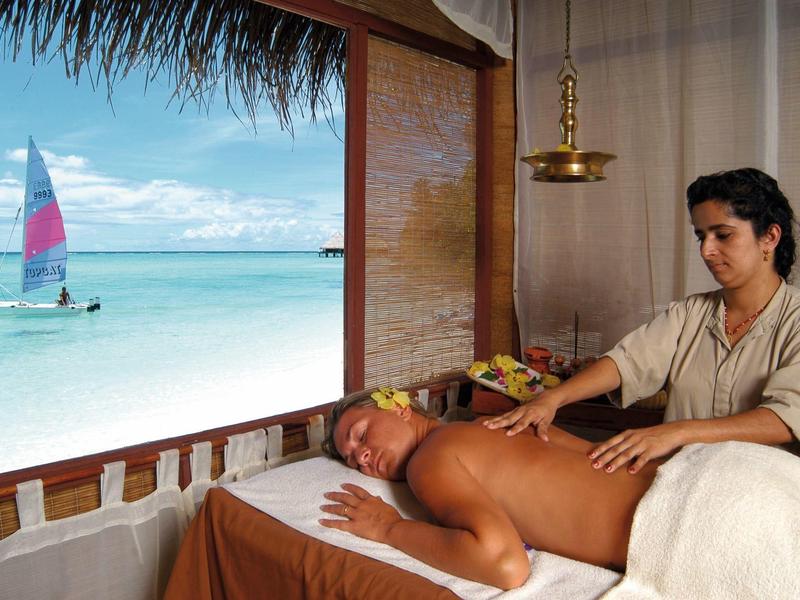 Massage in einem offenen Raum mit Blick auf türkisfarbenes Meer und Segelboot bei klarem Himmel.