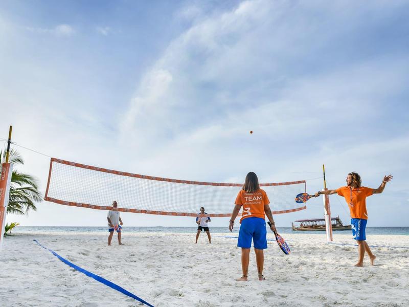 Menschen spielen Volleyball am Strand, blauer Himmel, weiße Sandfläche, entspannte Atmosphäre.