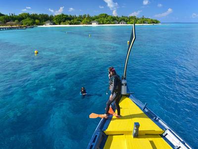 Klare blaue Meereswasser, Gelbes Boot und zwei Taucher nahe einer tropischen Insel mit Grün und Sandstrand.