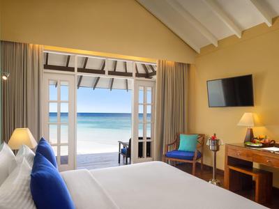 Hell eingerichtetes Hotelzimmer mit Meerblick, Bett, Stuhl, Schreibtisch und Fernseher an der Wand.