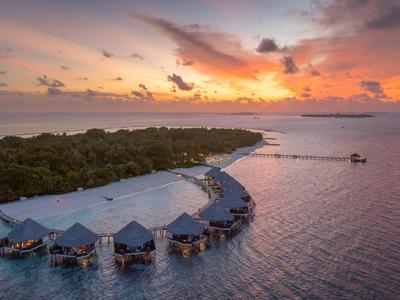 Sonnenuntergang über einer Insel mit Wasserbungalows, ruhigem Meer und Wolken am Himmel.