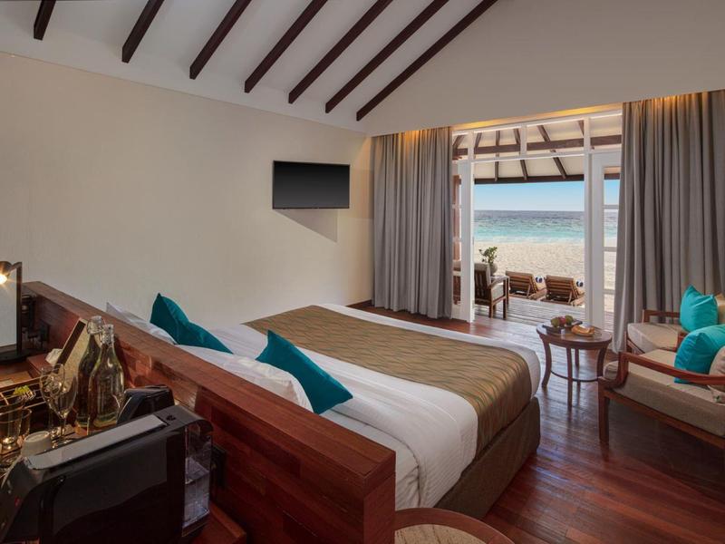 Chambre d'hôtel confortable avec poutres en bois, grand lit et vue sur la mer.