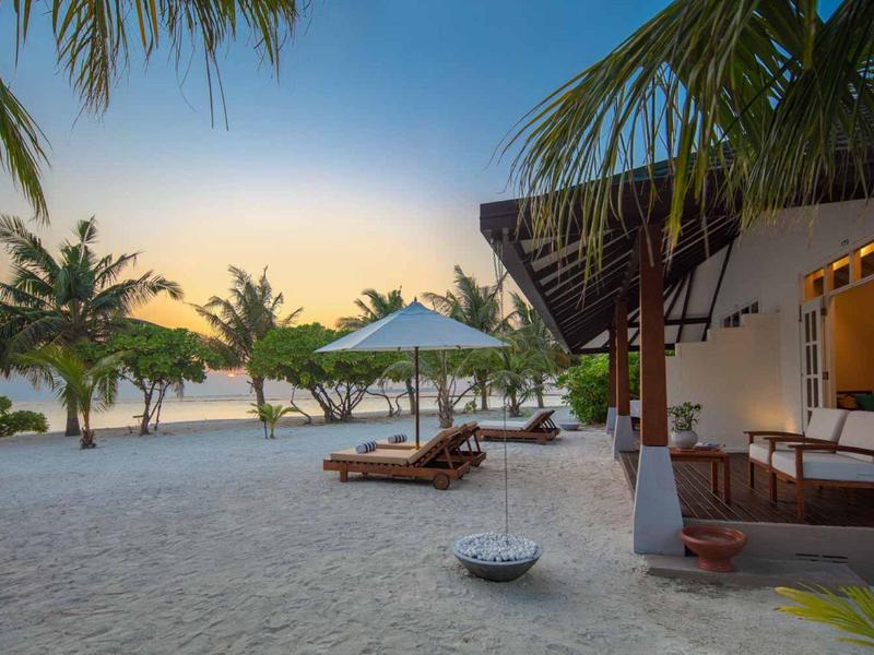 Bungalow de plage avec hamac et chaises longues sur une plage paisible au coucher du soleil.