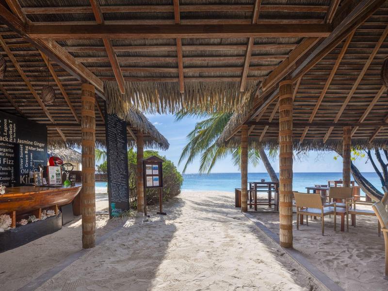 Restaurant de plage ouvert avec vue sur la mer et tables sous un toit de chaume.