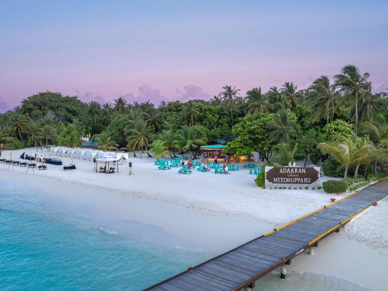 Station balnéaire avec sable blanc, eau turquoise et palmiers au coucher du soleil.