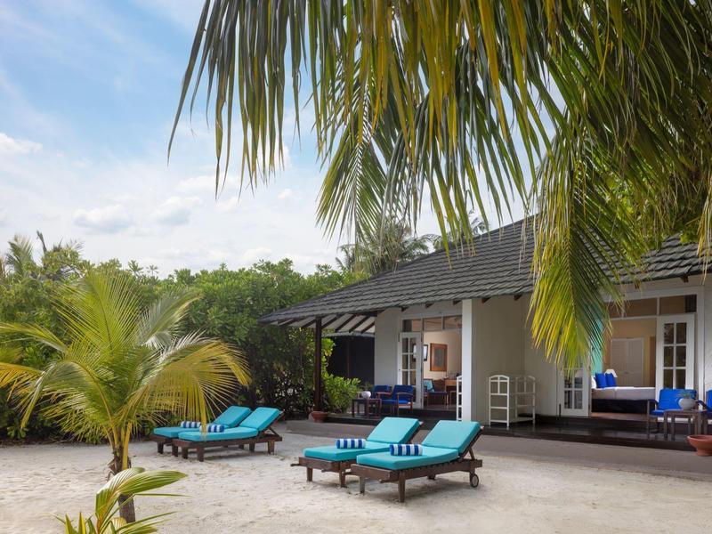 Villa de plage avec chaises longues bleues et palmiers sous un ciel clair