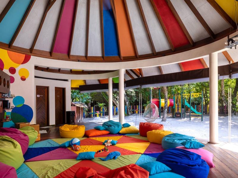 Espace lounge coloré avec coussins sous un toit rond dans une station tropicale.