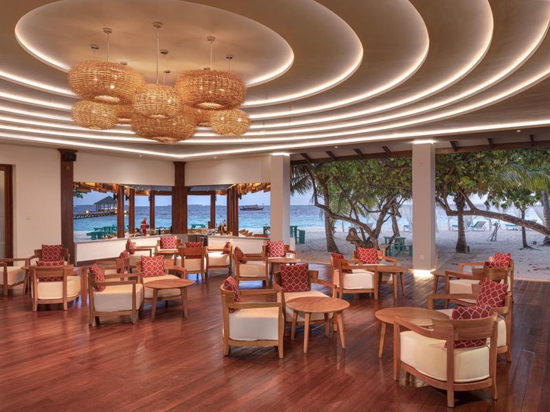 Espace lounge élégant d'hôtel avec sol en bois et vue sur l'océan au coucher du soleil.