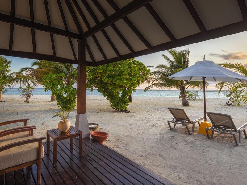 Terrasse couverte avec sièges et chaises longues sur la plage au coucher du soleil.