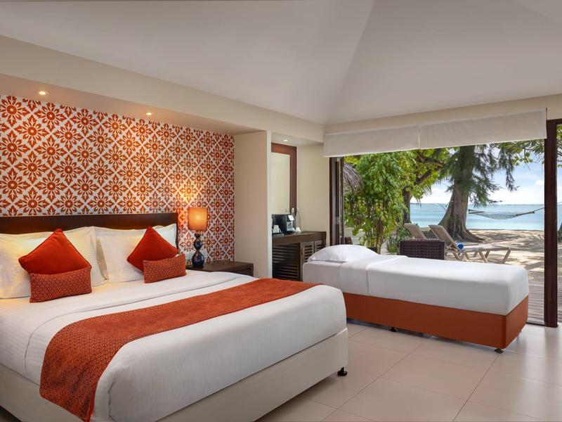 Hotelzimmer mit großem Bett, Sofabett, orangener Dekoration, Fenster mit Meerblick und Palme draußen.