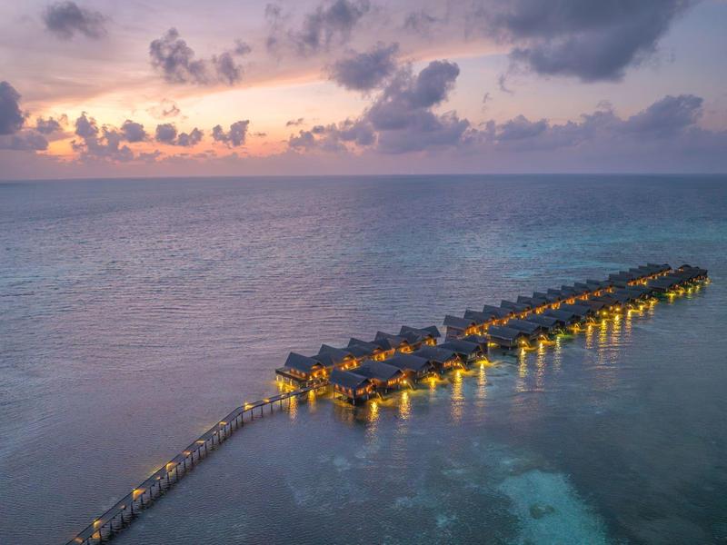 Dämmerung über ruhigem Meer mit beleuchteten Wasserbungalows auf langem Steg.