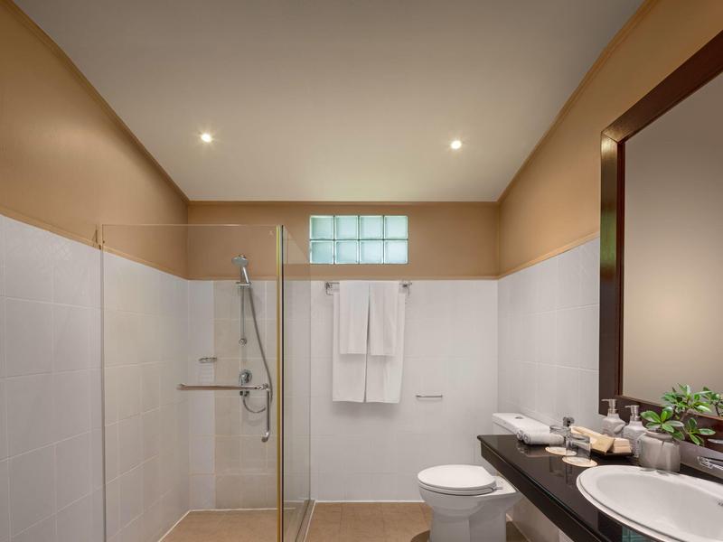 Modernes Badezimmer mit beiger Wandfarbe, Glasdusche, weißen Fliesen, Toilette und Waschbecken auf dunkler Ablage.