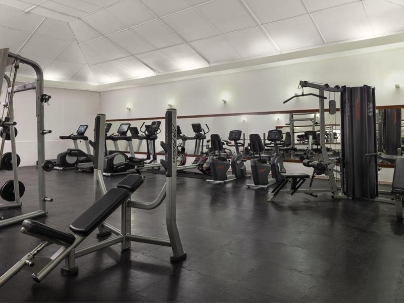 Weitläufiges Fitnessstudio mit verschiedenen Trainingsgeräten und Spiegelwand in hell beleuchtetem Raum.