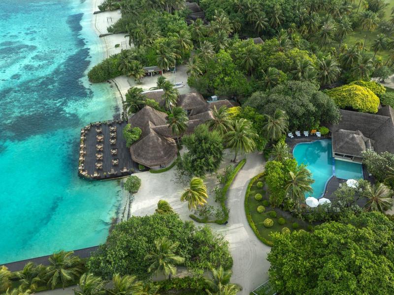 Tropische Insel mit türkisblauem Wasser, Palmendächern, Pools und dichtem grünem Pflanzenbewuchs.