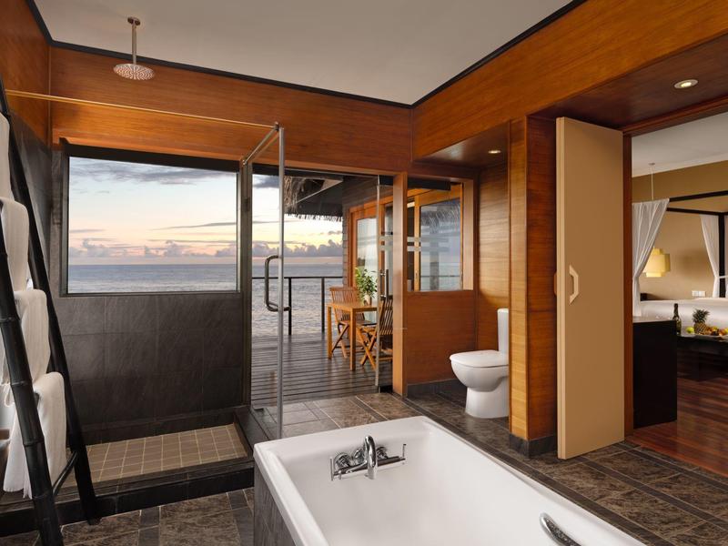 Moderner Badbereich mit freistehender Badewanne, Holzdecke und Blick auf Balkon mit Stühlen und Tisch.