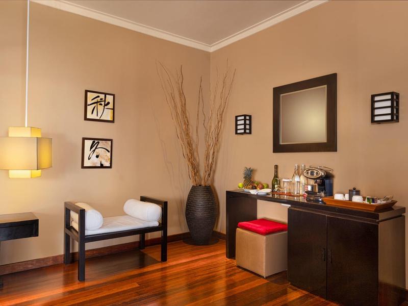 Gemütlicher Raum mit Holzboden, Stuhl, Hocker, großem Spiegel und dekorativem Vase-Arrangement.