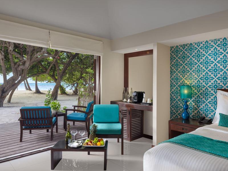 Modernes Schlafzimmer mit türkisfarbenem Akzent, Blick auf Terrasse und Strand mit Palmen.