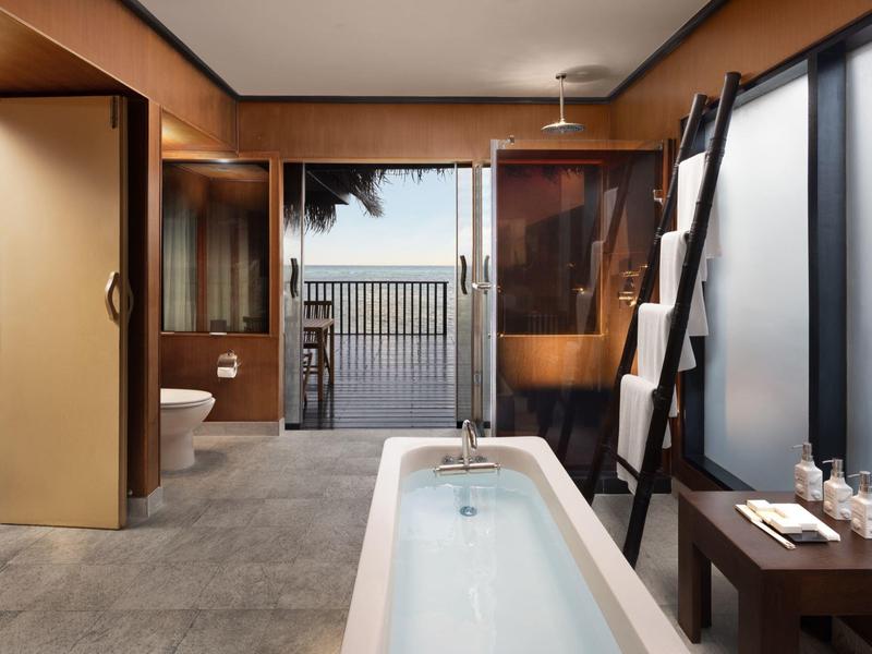 Moderner Holzbadraum mit freistehender Badewanne, großer Glasfront und Blick auf Meer und Terrasse.