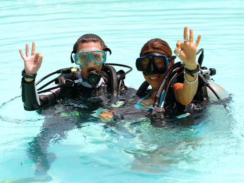 Zwei Taucher mit Masken und Anzügen zeigen im Wasser ein Handzeichen.