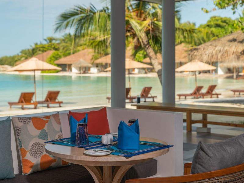 Ein gedeckter Tisch mit blauen Servietten vor Schwimmbad und Liegestühlen unter Sonnenschirmen.