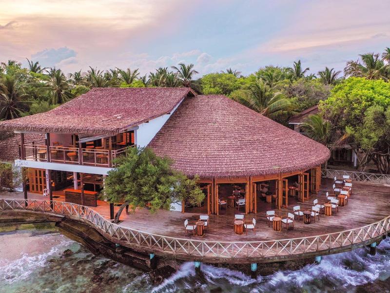 Großes Holzhaus am Wasser mit Terrasse und Stühlen, umgeben von viel grünem Palmenwald.