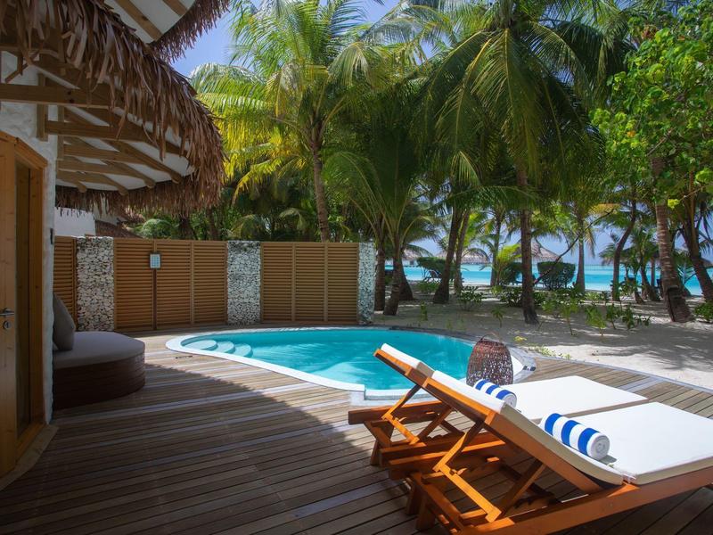 Terrasse mit Holzliege, Pool, Palmen und Blick auf das Meer bei sonnigem Wetter.