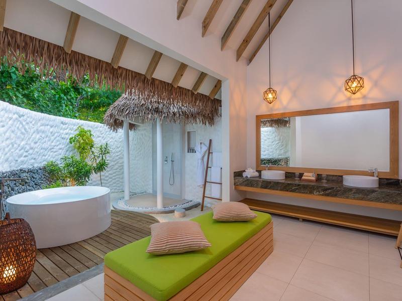 Moderner Wellnessbereich mit grünem Sitzpolster, runder Badewanne, Holzdach und großen Spiegeln.