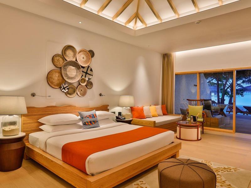 Modernes Schlafzimmer mit großem Bett, orangener Bettdecke, Holzdekor und Blick auf Terrasse bei Abendlicht.