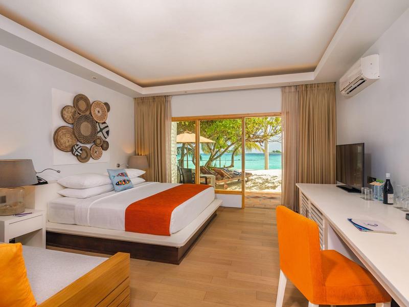 Helles Hotelzimmer mit Doppelbett, orange Akzenten, Schreibtisch, Balkon und Poolblick.