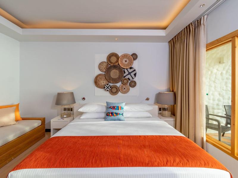 Gemütliches Schlafzimmer mit großem Bett, orangefarbenen Akzenten und Holzmöbeln, lichtdurchflutet.