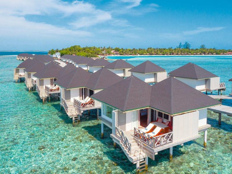 Reihen über Wasser gebaute Bungalows mit dunklen Dächern in klarem türkisfarbenem Meer und blauem Himmel.