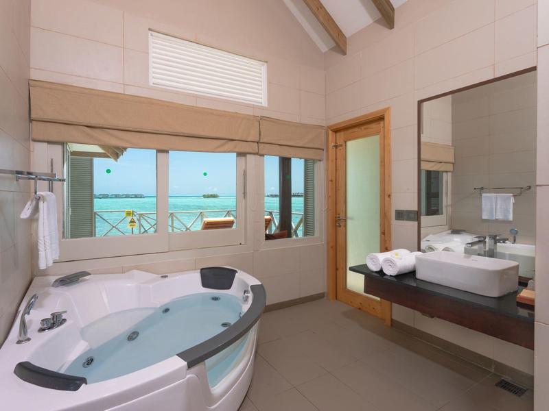 Helles Badezimmer mit Whirlpool-Badewanne, großem Spiegel und Fenster mit Meerblick.