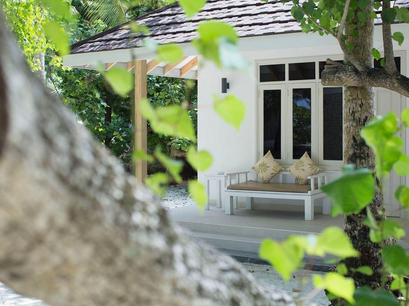 Cozy patio with sofa at a white house surrounded by green trees.