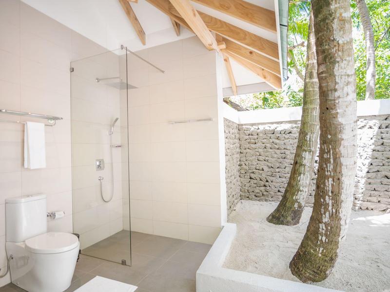 Modern bathroom with freestanding toilet and walk-in shower under wooden beam ceiling.