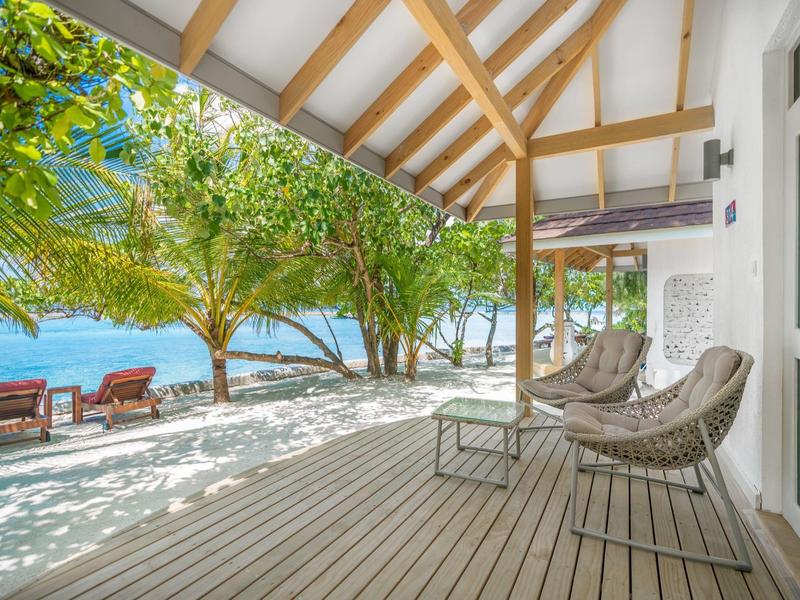 Veranda with chairs overlooking the beach with loungers and sea under blue sky.