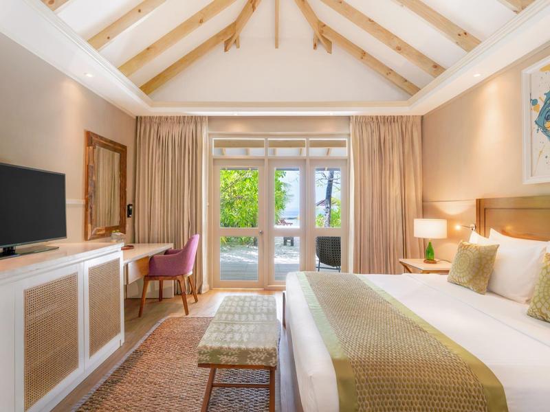 Bright hotel room with double bed, TV, desk, and terrace view through glass sliding door.