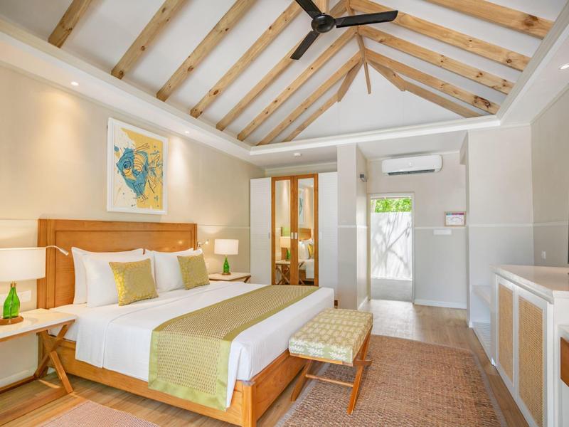 Bright hotel room with wooden beam ceiling, large bed, and modern decor.