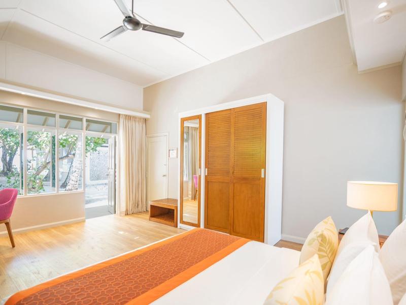 Bright hotel room with large bed, wardrobe, and outdoor terrace overlooking greenery.