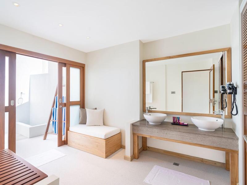 Bright bathroom with double sinks, large mirror, and bench by the door to the balcony.