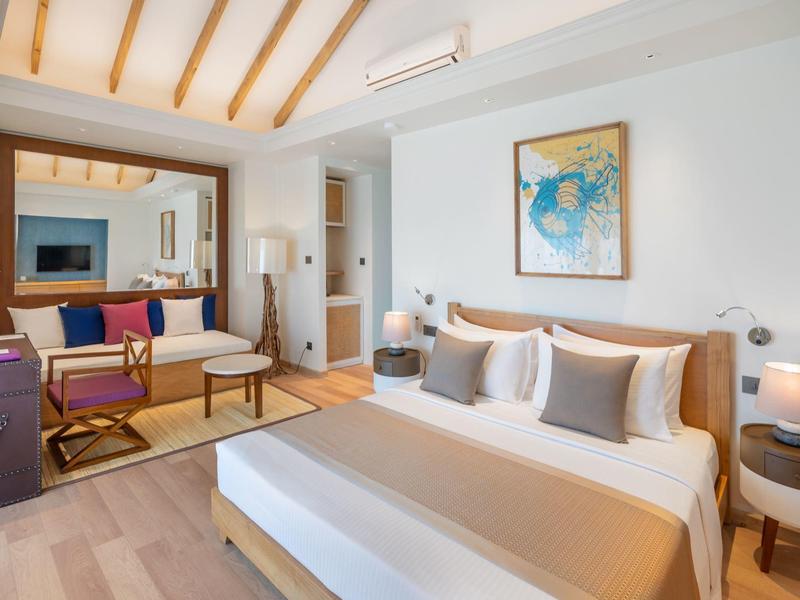 Modern hotel room with double bed, sofa, TV, and artwork on the wall.