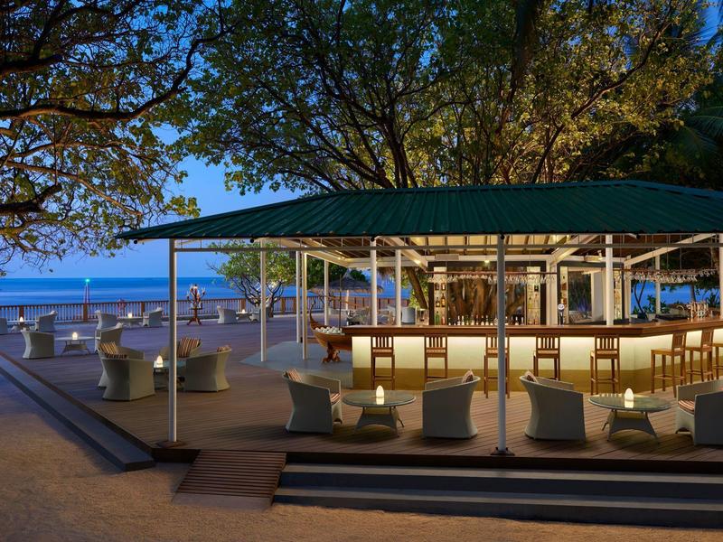 Evening beach bar with seating under trees and a view of the sea.