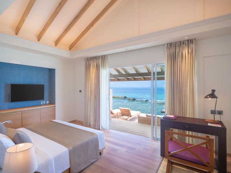 Modern hotel room with canopy bed, desk, and sea view through large windows.