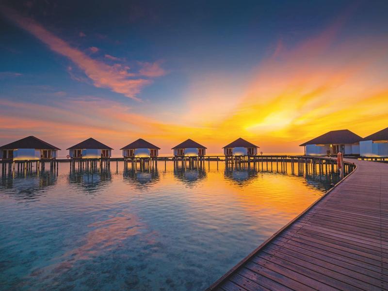 Overwater bungalows at sunset with a pier on the right side.