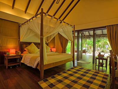 Pohodlný hotelový pokoj s postelí s baldachýnem, dřevěnou podlahou a přístupem na terasu.